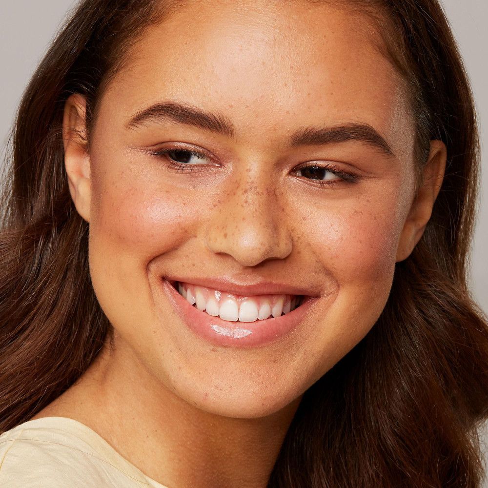 Portrait d'une femme souriante. Sourcils naturels, teint. Aucun produit visible.