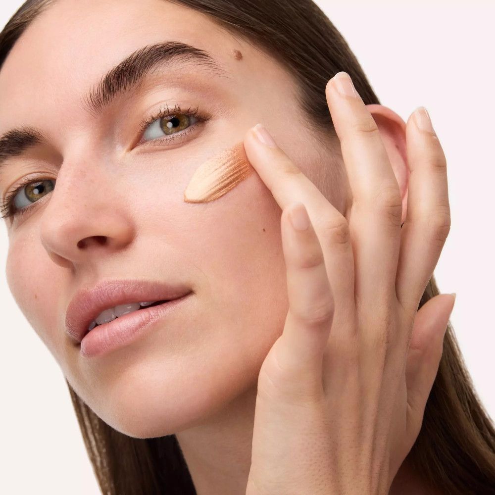 Femme appliquant Bronze Glow Grip Primer. Doigts touchant le visage. Peau avec primer.