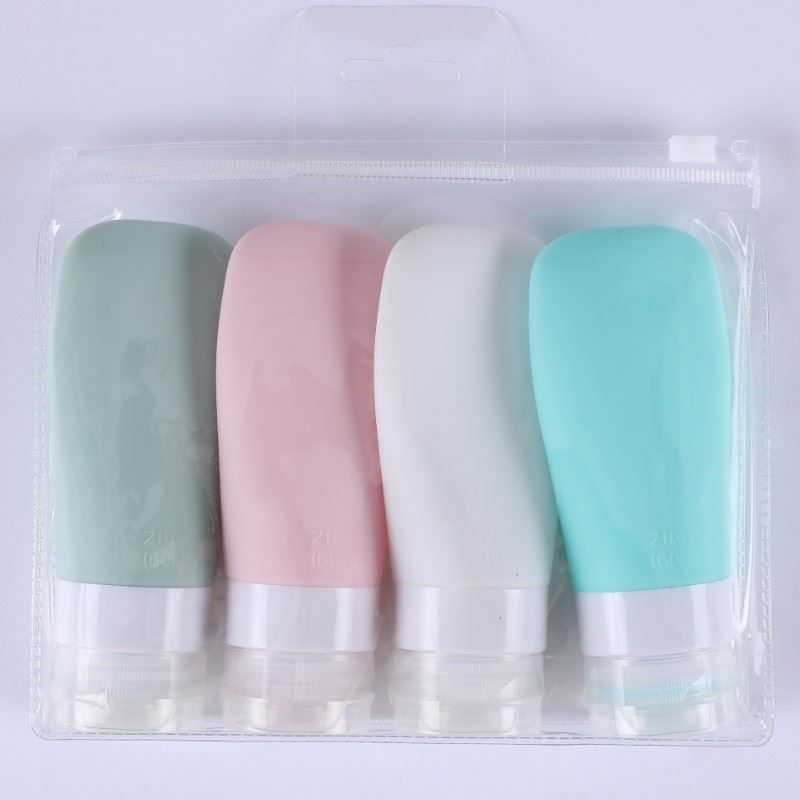 Quatre flacons de voyage colorés dans un sac transparent. Couleurs : vert, rose, blanc et turquoise. Avec couvercle blanc.