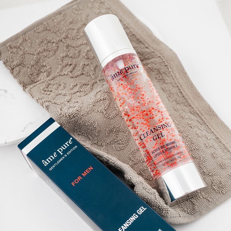 Un flacon de gel nettoyant avec particules rouges repose sur une serviette à côté d'une boîte ouverte.
