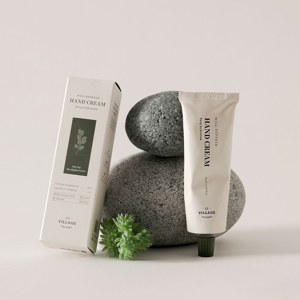 Tube de crème et boîte à côté de pierres. Inscription: WILL REFRESH HAND CREAM, VILLAGE 11 FACTORY. Boîte avec motif de feuilles.