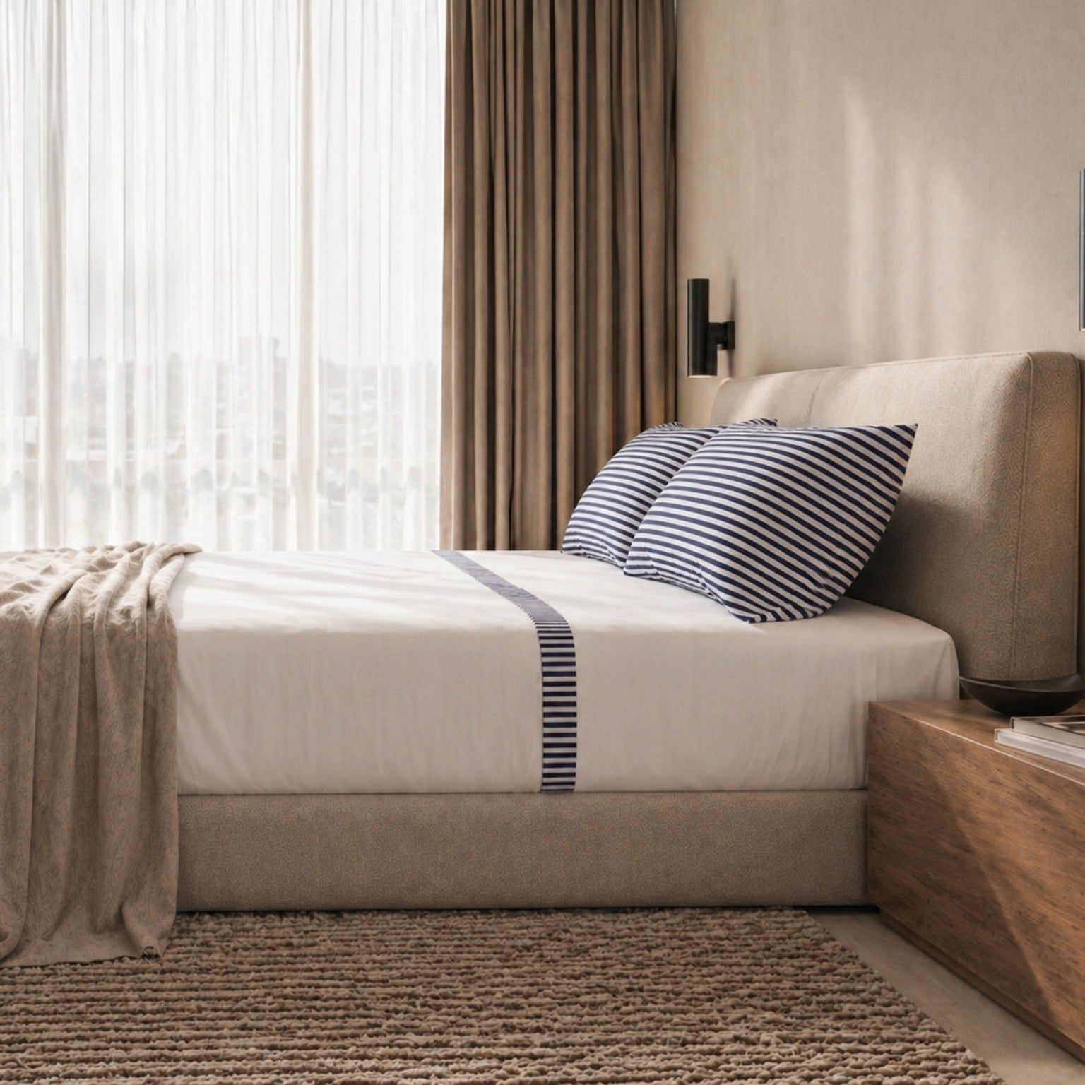 Opgemaakt bed met gestreept beddengoed en een deken.