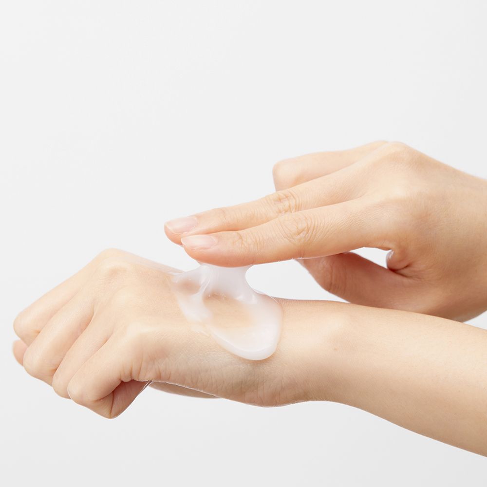 Mains appliquant un liquide transparent sur la peau. Fond blanc.