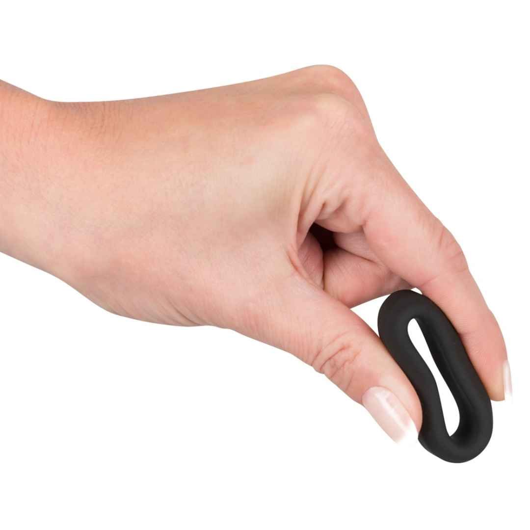 Main tenant une bague de pénis noire flexible en silicone.
