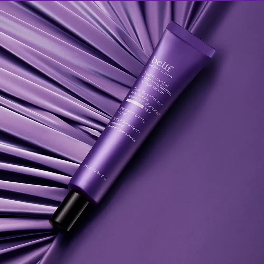 Paarse tube met zwarte dop. Opschrift: belif, Youth creator - age knockdown V eye serum. Op paarse achtergrond.