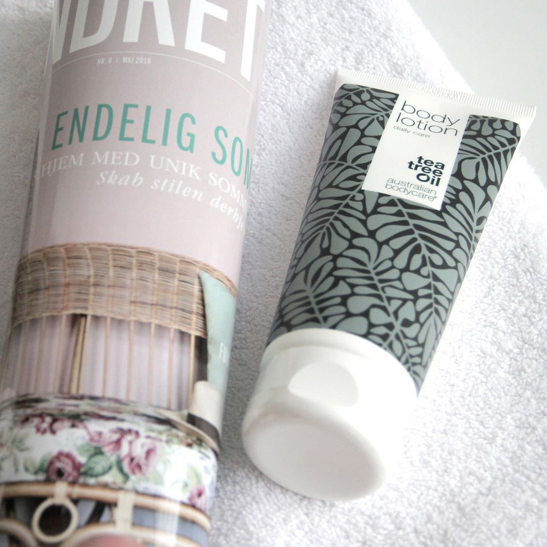Body Lotion tube naast tijdschrift. Witte tube met grijze bladeren. Tekst: Tea Tree Oil, Australian Bodycare.