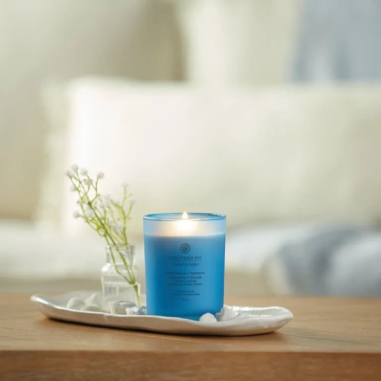 Bougie bleue allumée sur plateau. Accompagnée d'un vase avec fleurs et pierres. Arrière-plan: canapé.