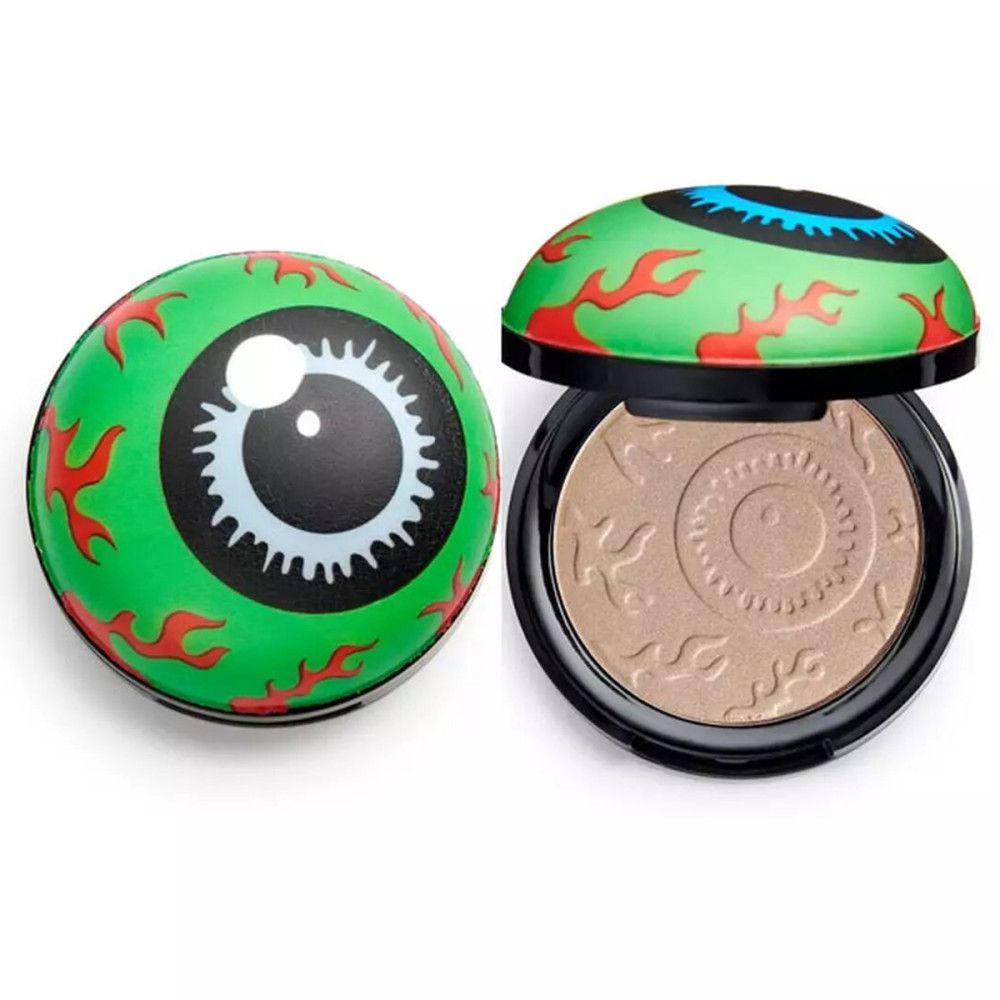 Highlighter rond avec design d'œil vert. Poudre beige avec motif en relief. Boîtier noir avec couvercle vert.