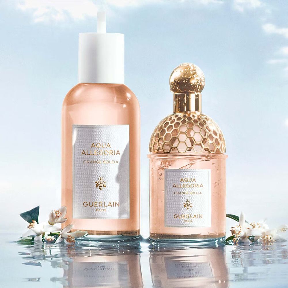 Deux flacons de parfum à côté de fleurs. Flacons avec étiquettes Aqua Allegoria, Orange Soleia et Guerlain. Fond: eau.