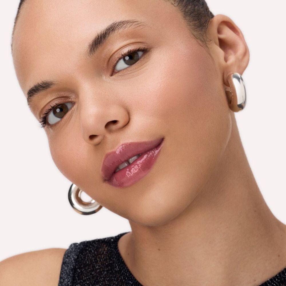 Portret van een vrouw met aangebrachte Catrice Peptide Bliss Glossy Lip Balm. Glanzende lippen, zilveren oorbellen.