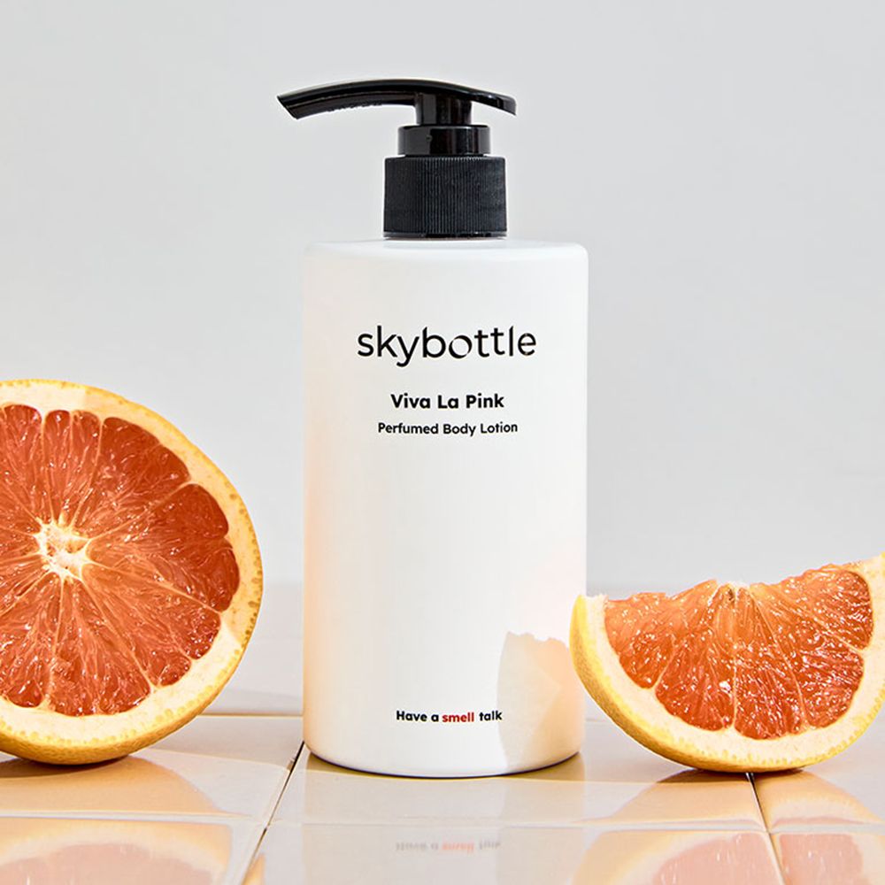 Witte fles met zwarte pomp en twee helften van een grapefruit. Opschrift: skybottle, Viva La Pink, Perfumed Body Lotion.