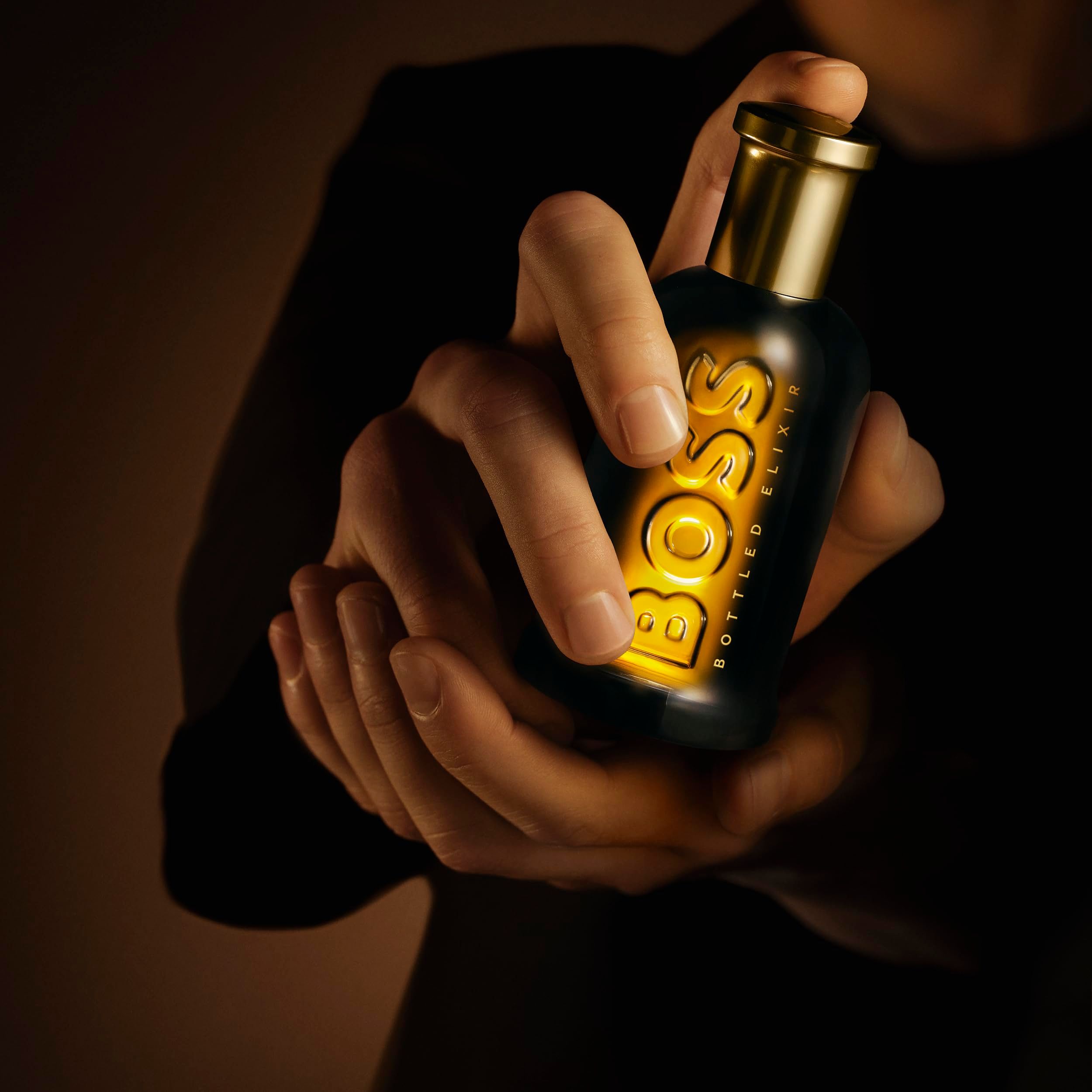 Mains tenant un flacon lumineux Hugo Boss Bottled Elixir.