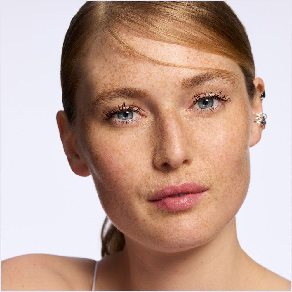 Portrait d'une femme avec des taches de rousseur et du baume à lèvres. Les lèvres sont teintées de rose.