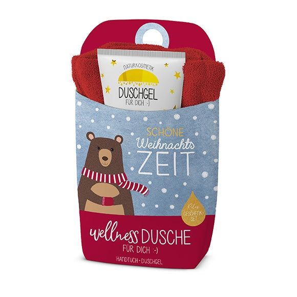 Coffret cadeau douche bien-être. Contient une serviette rouge, un gel douche et un emballage cadeau avec un ours et l'inscription 'Schöne Weihnachtszeit'.