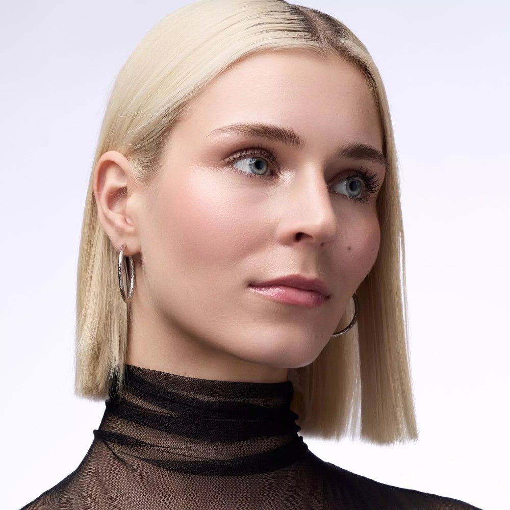 Portrait d'une femme aux cheveux blonds. Elle porte des créoles argentées. Maquillage appliqué, dont un highlighter.