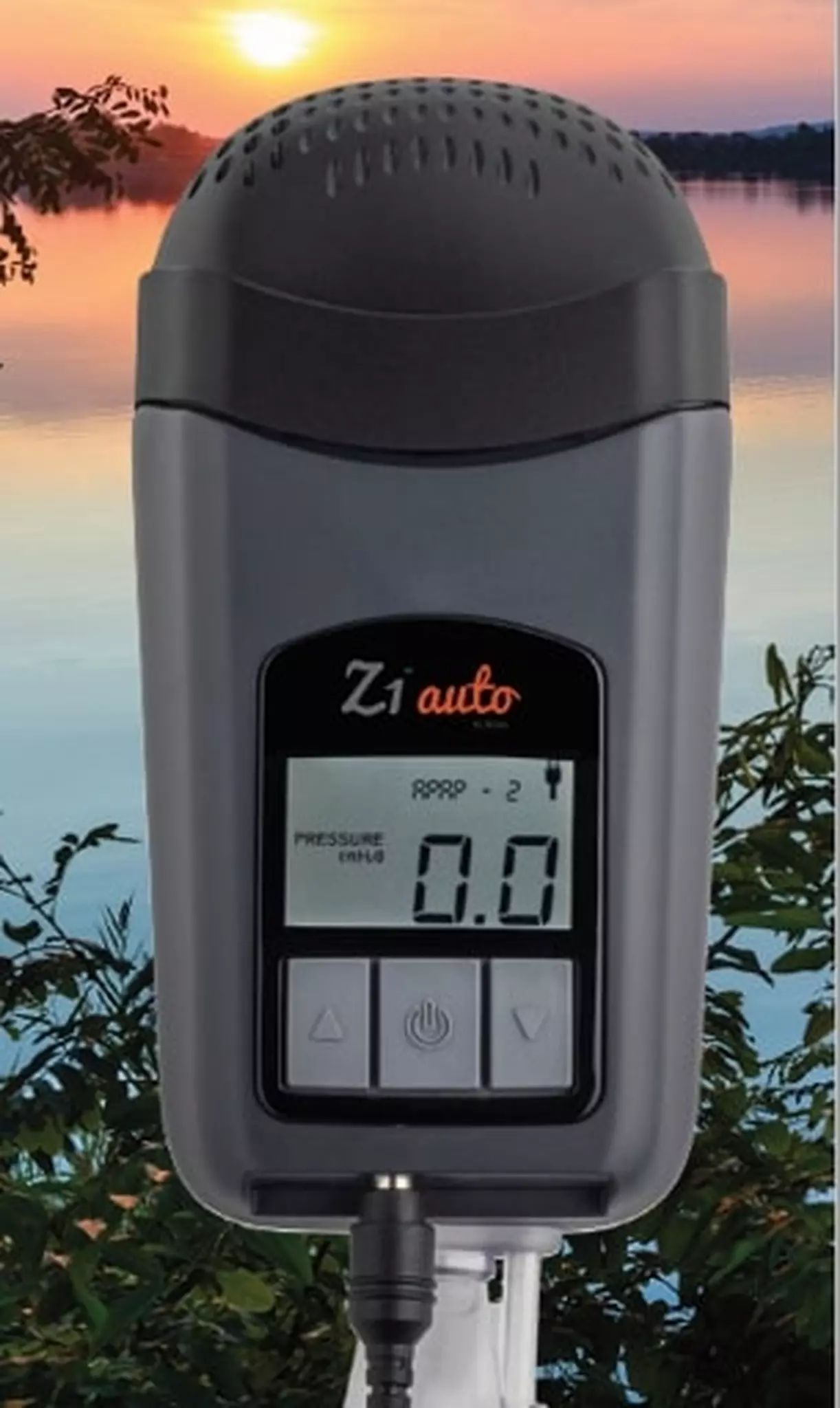Appareil CPAP de voyage gris avec écran, affiche "0.0", devant un lac et des arbres.