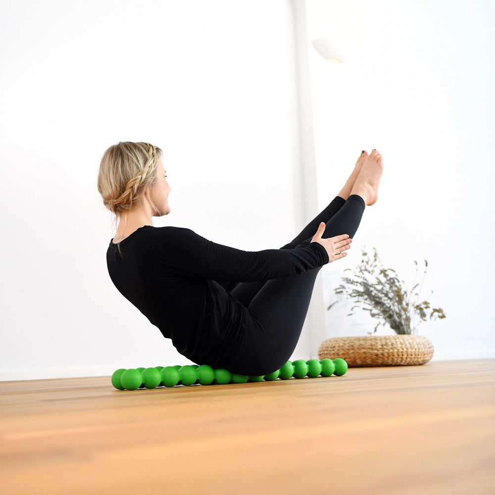 Een vrouw doet een oefening op een groene Spinefitter. De achtergrond is licht en houten.