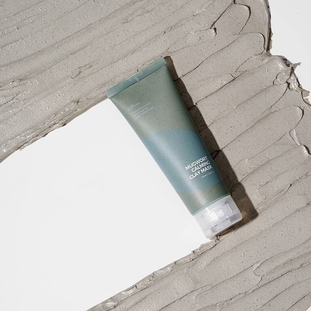 Tube op grijze klei. Opschrift: MUGWORT CALMING CLAY MASK. Transparante sluiting. Cosmetisch product.