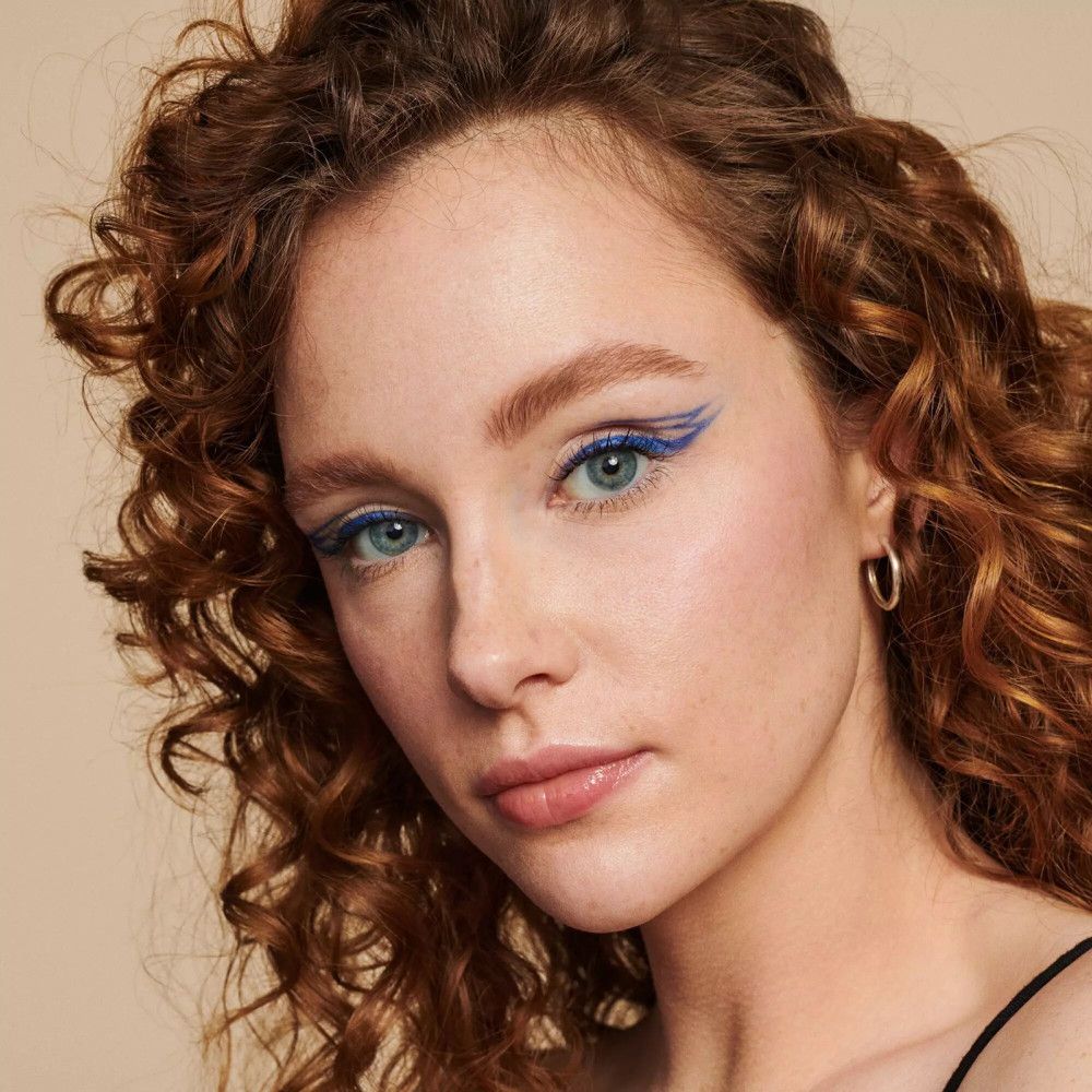 Portrait d'une femme avec eye-liner bleu. Cheveux bouclés, créoles argentées. Teint clair.