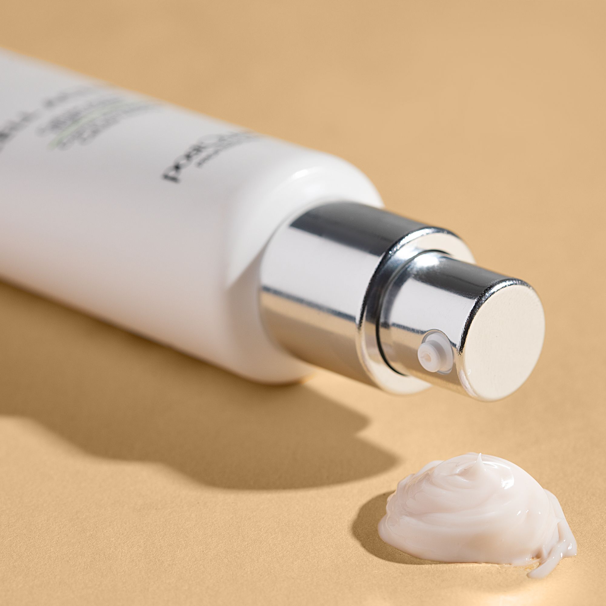 Witte fles met zilveren pomp. Klodder crème op beige achtergrond.