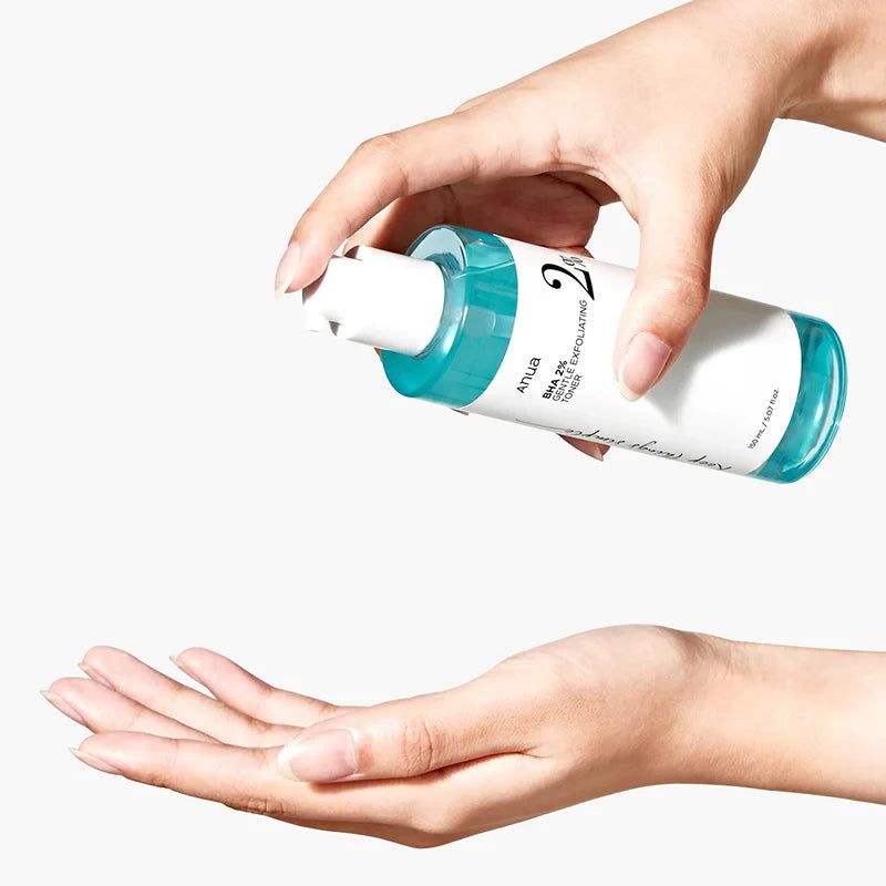 Handen houden een tonerfles vast. Opschrift: Anua BHA 2% Gentle Exfoliating Toner. Vloeistof wordt in de handpalm gegoten.