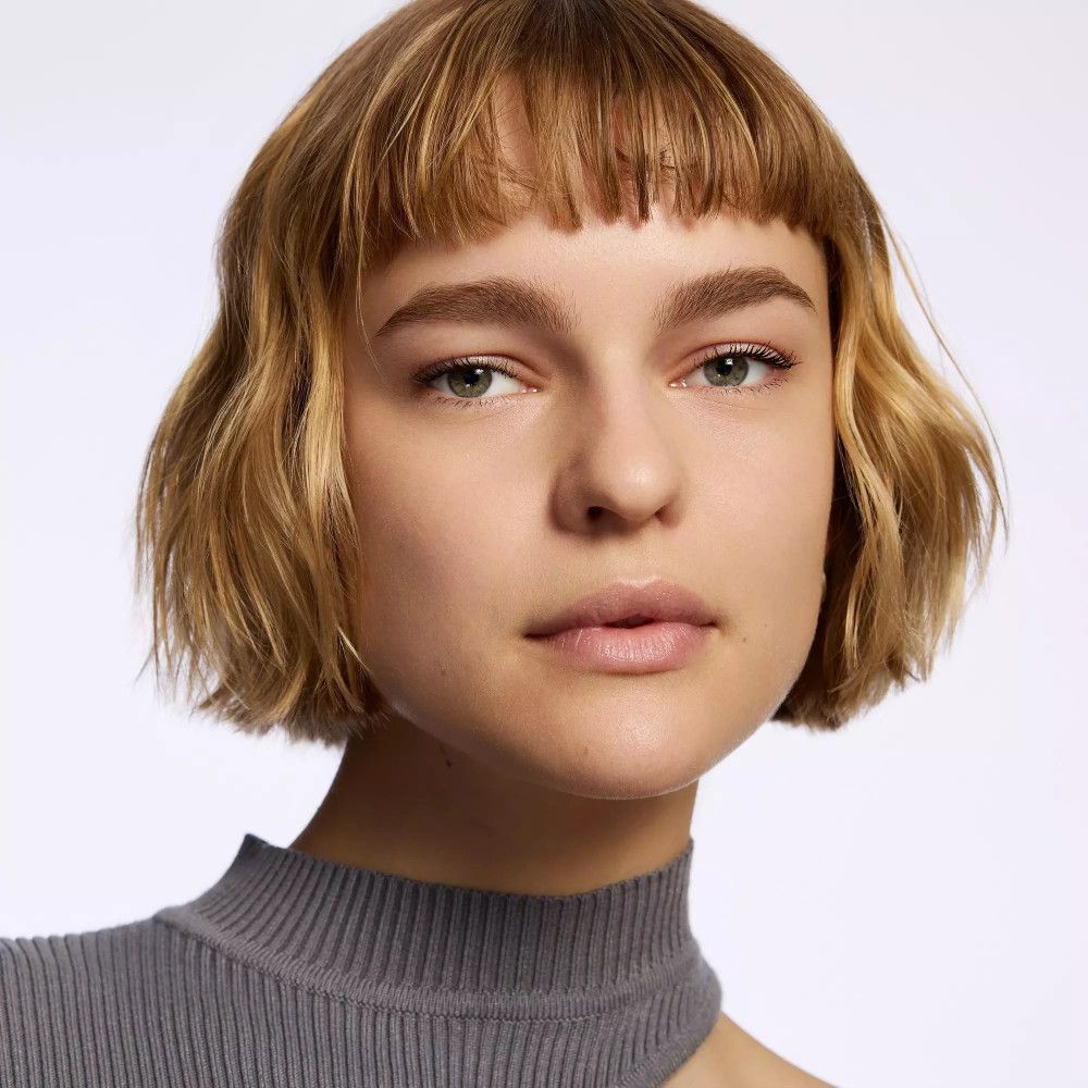 Portrait d'une femme aux cheveux blonds et haut gris. Elle regarde la caméra.