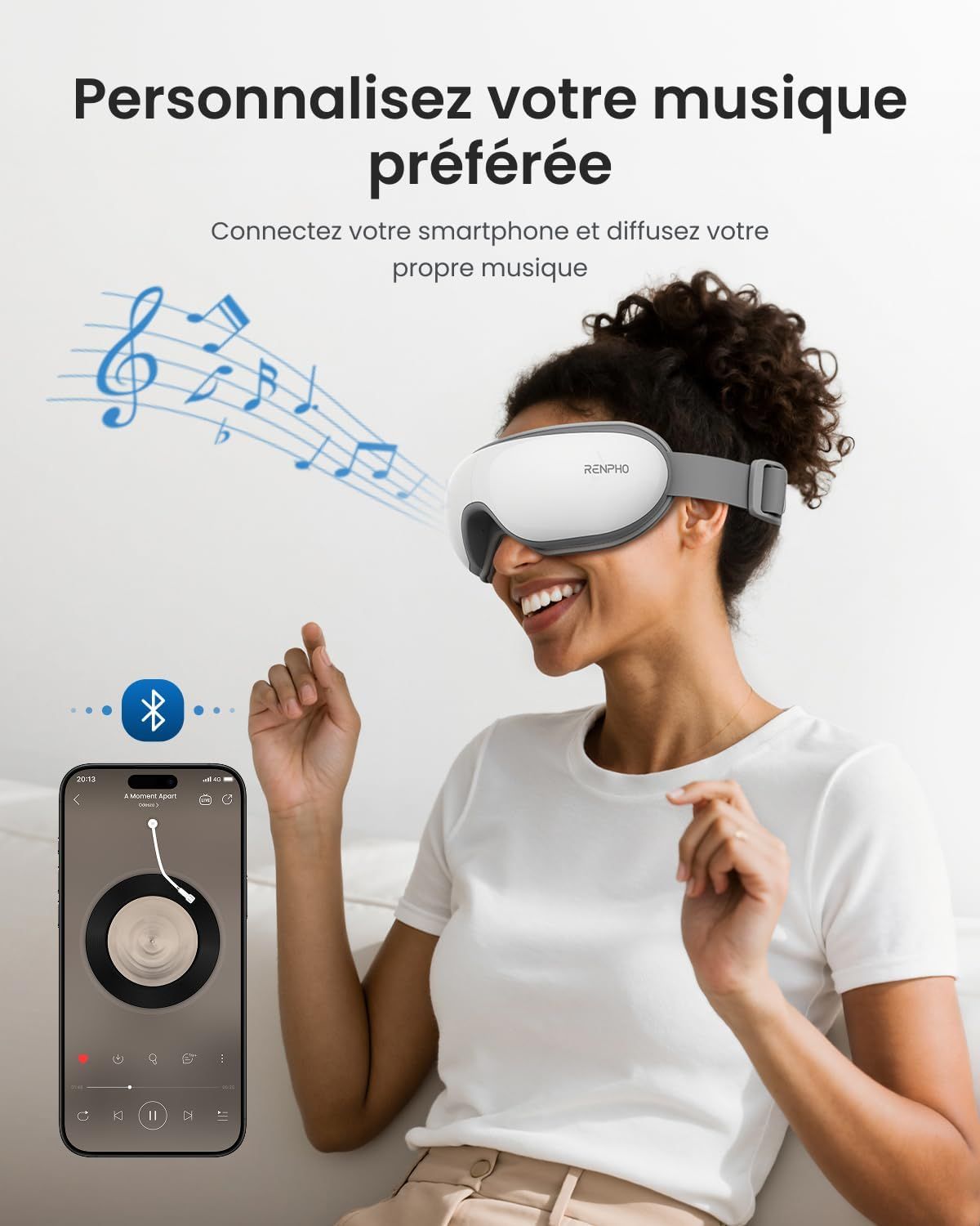Une femme porte des lunettes de massage oculaire blanches et grises connectées par Bluetooth à un smartphone jouant de la musique.