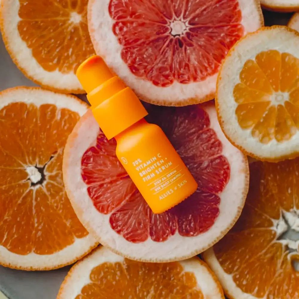 Oranje serumflesje op grapefruit- en sinaasappelschijfjes. Opschrift: 20% Vitamin C Brighten + Firm Serum. Merk: Allies of Skin.