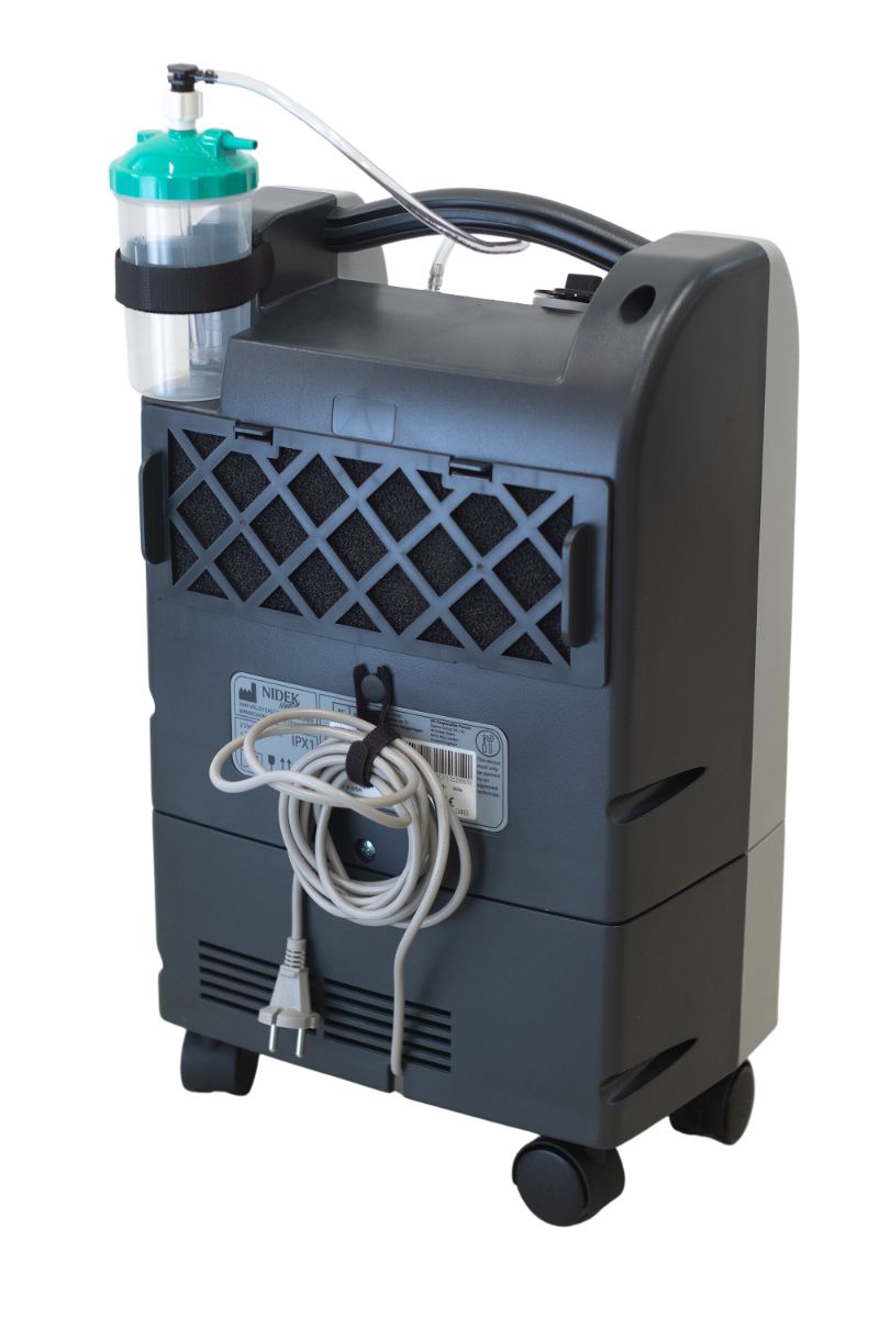 Achterkant van een Nidek Nuvo Lite zuurstofconcentrator met wielen, snoer en bevochtigingsfles.
