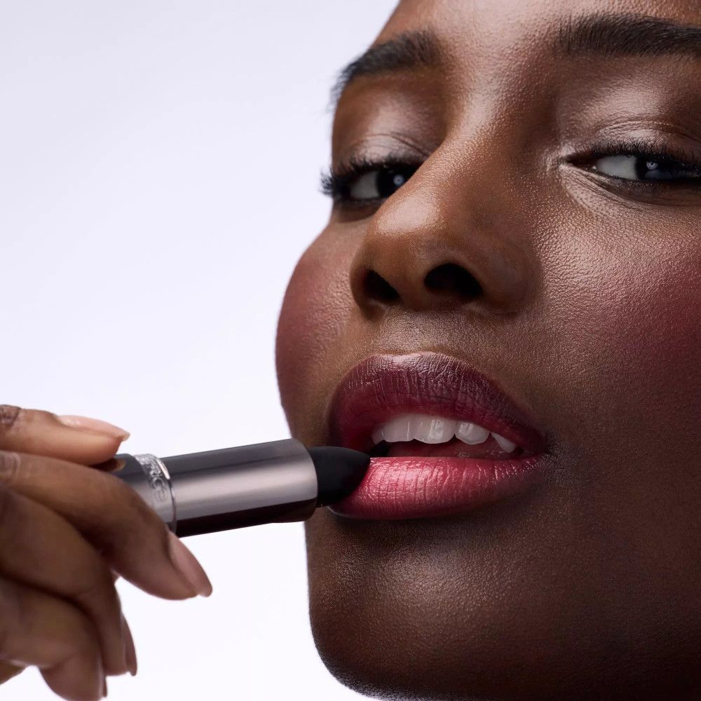 Persoon brengt lippenstift aan. De lippen zijn donkerrood. De lippenstift is zilverkleurig. Merk: Catrice.