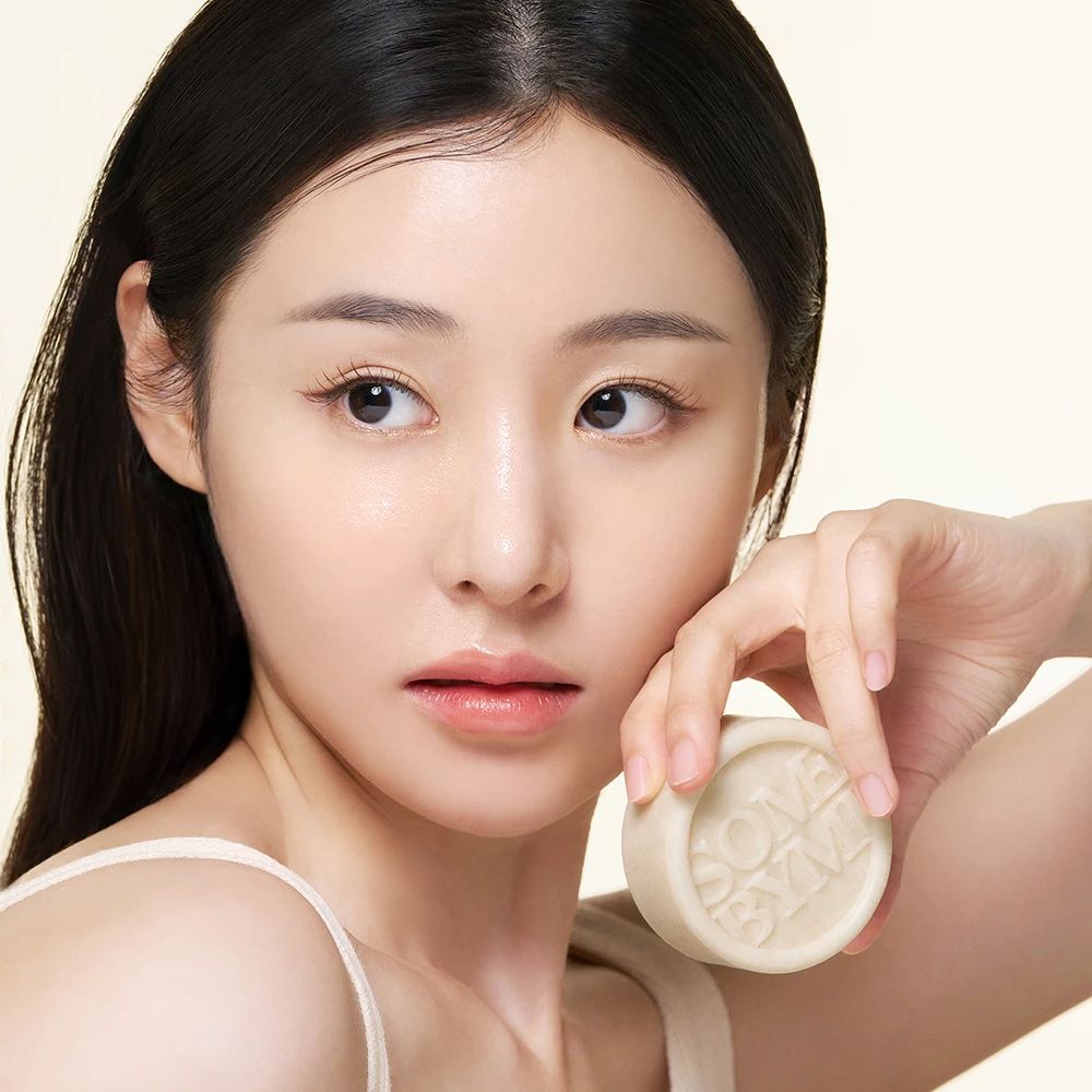 Une femme tient un savon rond avec le texte SOME BYMI. Elle touche son visage.