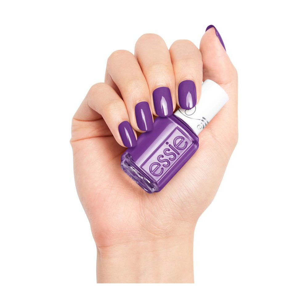 Hand met gelakte nagels en nagellakflesje. Flesje met witte dop, paarse lak, Essie-logo. Nagels in bijpassende kleur.