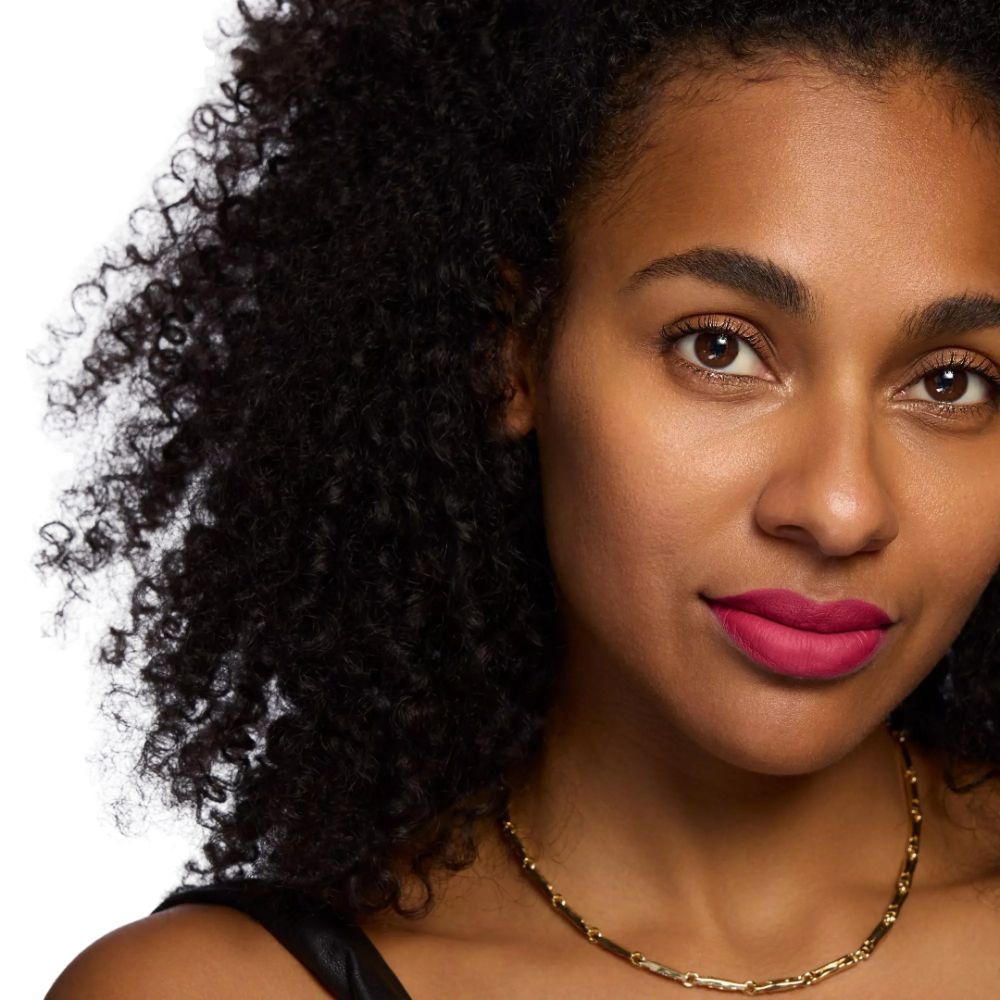 Portrait d'une femme à la peau foncée. Elle porte un rouge à lèvres rouge. Collier doré.