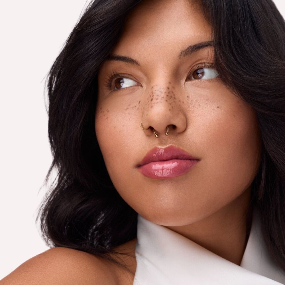 Portret van een vrouw met donker haar en sproeten. Ze draagt roze lipgloss. Zijwaartse blik.