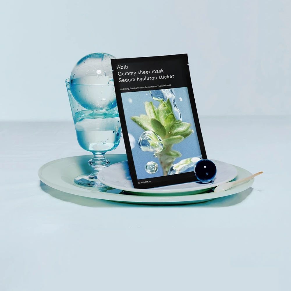 Abib Gummy Sheet Mask Sedum Hyaluron Sticker sur une assiette avec verre et eau.