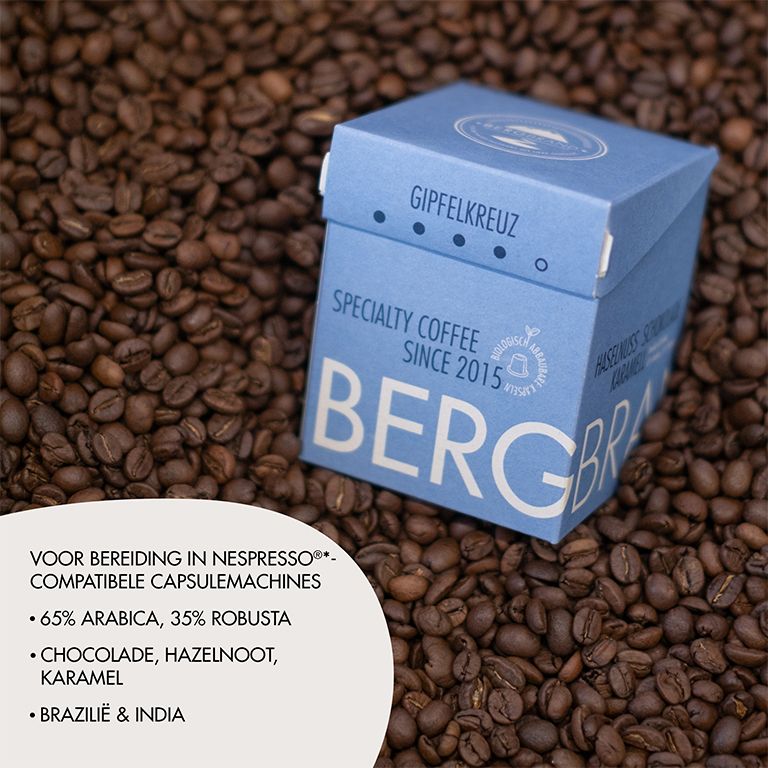 Blauwe doos met koffiecapsules op koffiebonen. Tekst: BERGBRAND, Gipfelkreuz, Specialty Coffee. Tekst.