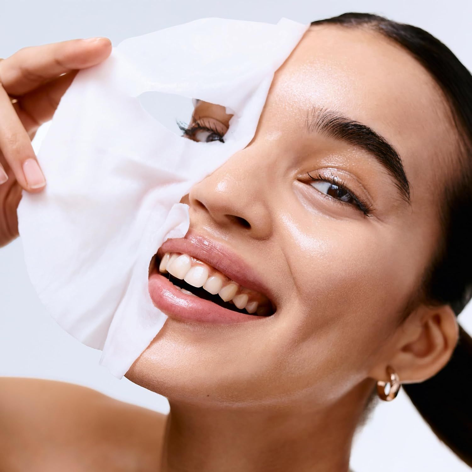 Femme tenant un masque en tissu devant son visage. Le masque couvre une moitié du visage. Elle sourit.