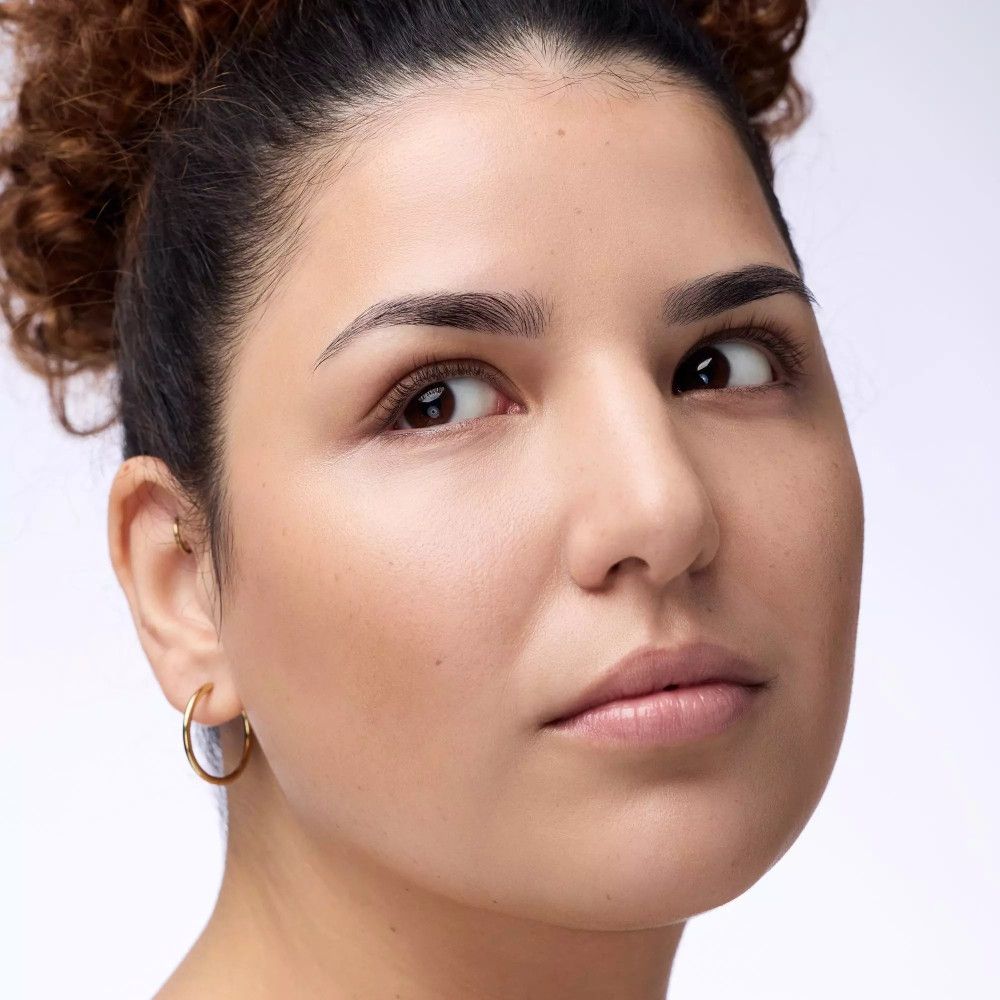 Portret van een vrouw met krullen. Ze kijkt opzij. Aangebracht product zichtbaar.