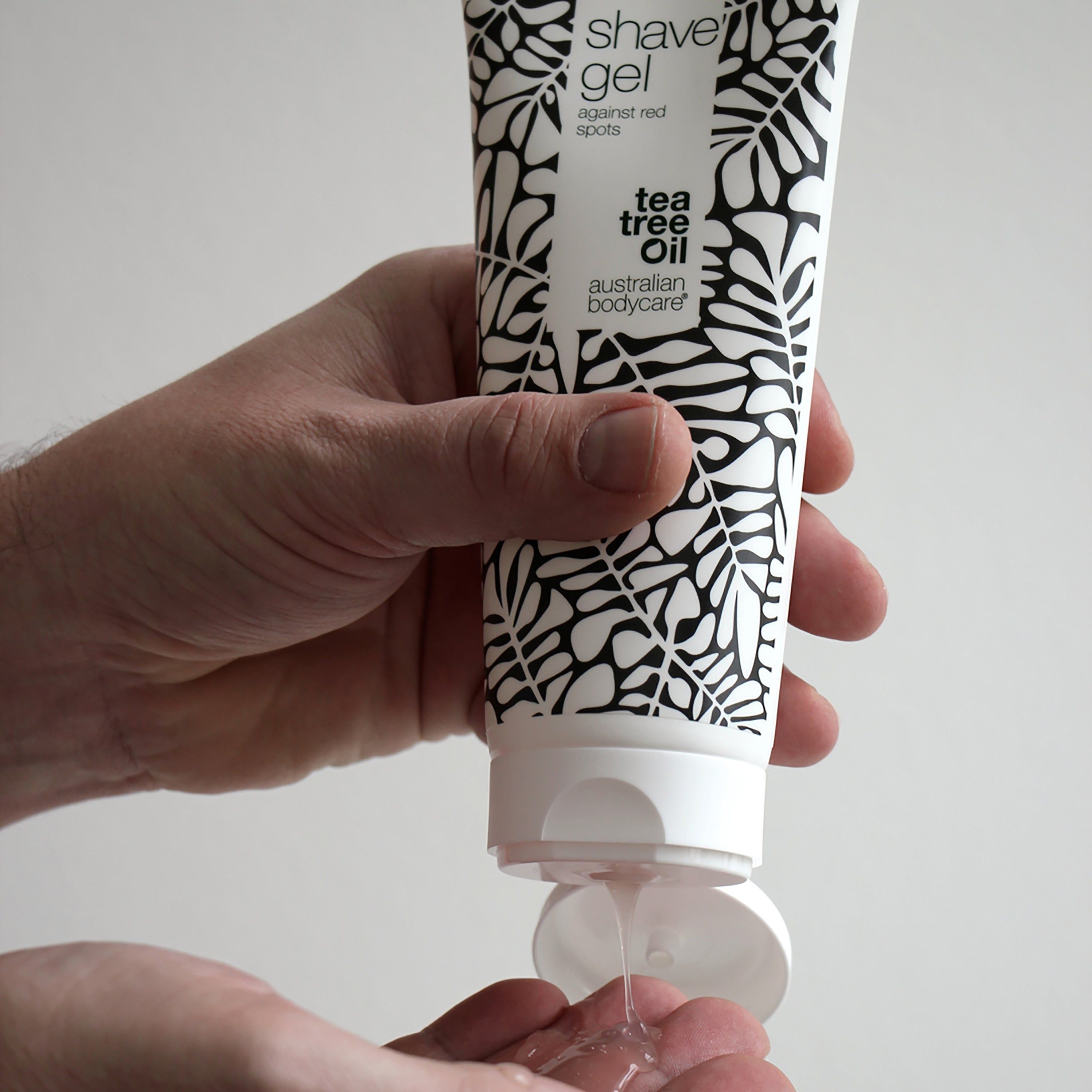 Personne tenant un tube de gel à raser. Le gel est pressé dans la main. Inscription: shave gel against red spots. Australian Bodycare.