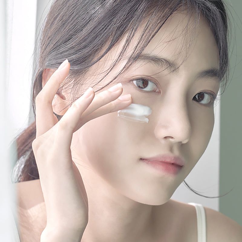 Close-up van een vrouw die lotion op haar gezicht aanbrengt. Geen verpakking zichtbaar.