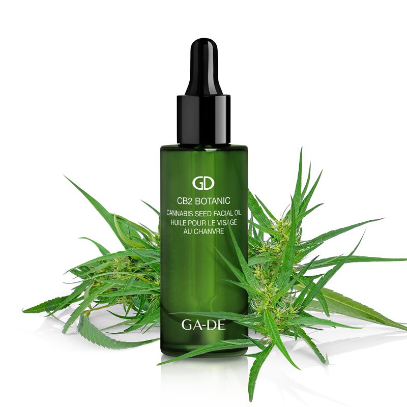 Flacon en verre vert avec compte-gouttes noir, entouré de feuilles de cannabis. Inscription: CB2 Botanic Cannabis Seed Facial Oil. Marque: GA-DE.