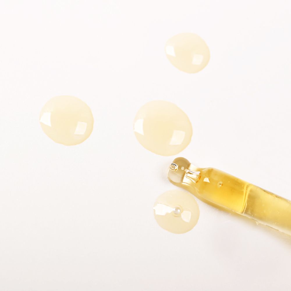 Close-up van oliedruppels en pipet. Heldere vloeistof. Pipet gevuld met olie. Achtergrond wit.