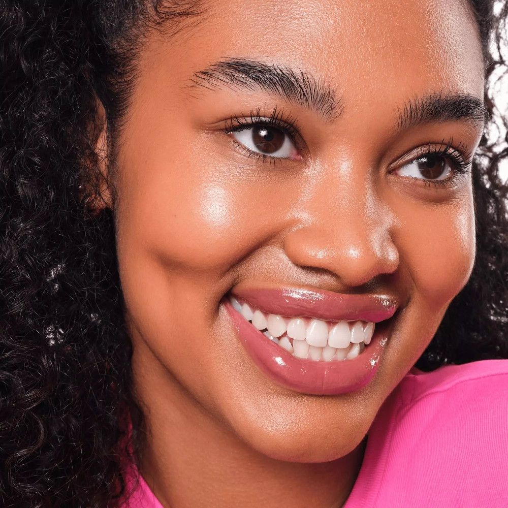 Portret van een vrouw met roze lipgloss. Ze glimlacht. Huid en lippen glanzen.