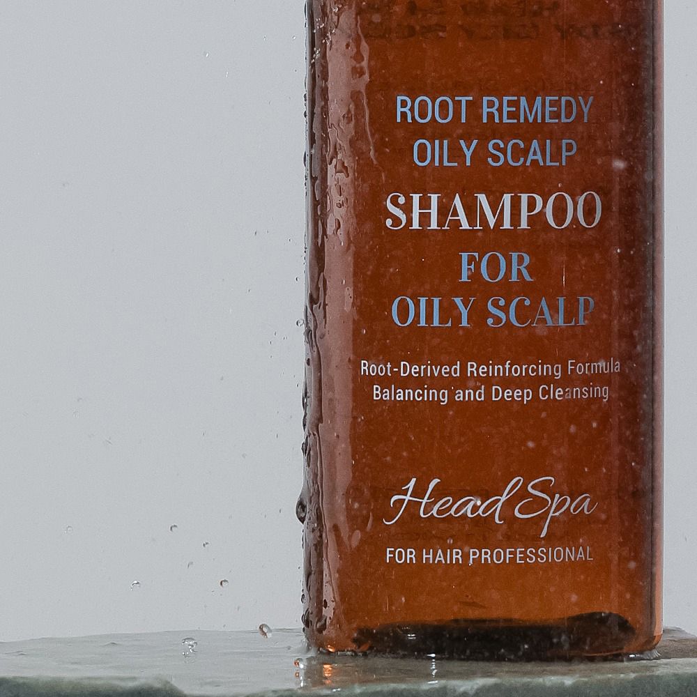 Gros plan sur le flacon de shampooing. Inscription : Root Remedy Oily Scalp Shampoo. Texte : For Oily Scalp, Head Spa. Gouttes d'eau.