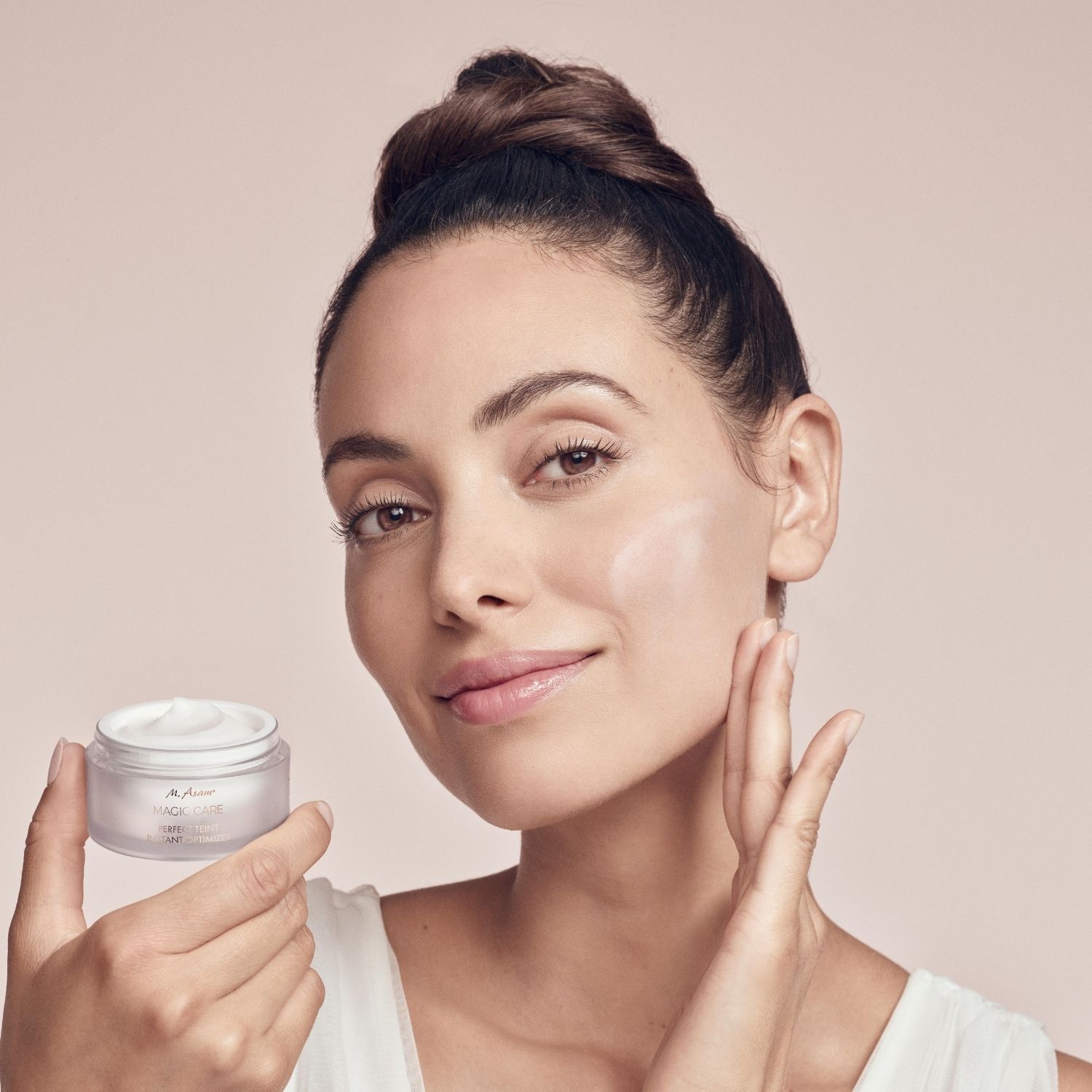 Vrouw houdt crèmepot vast. Brengt crème aan. Tekst: M. Asam MAGIC CARE PERFECT TEINT INSTANT OPTIMIZER.