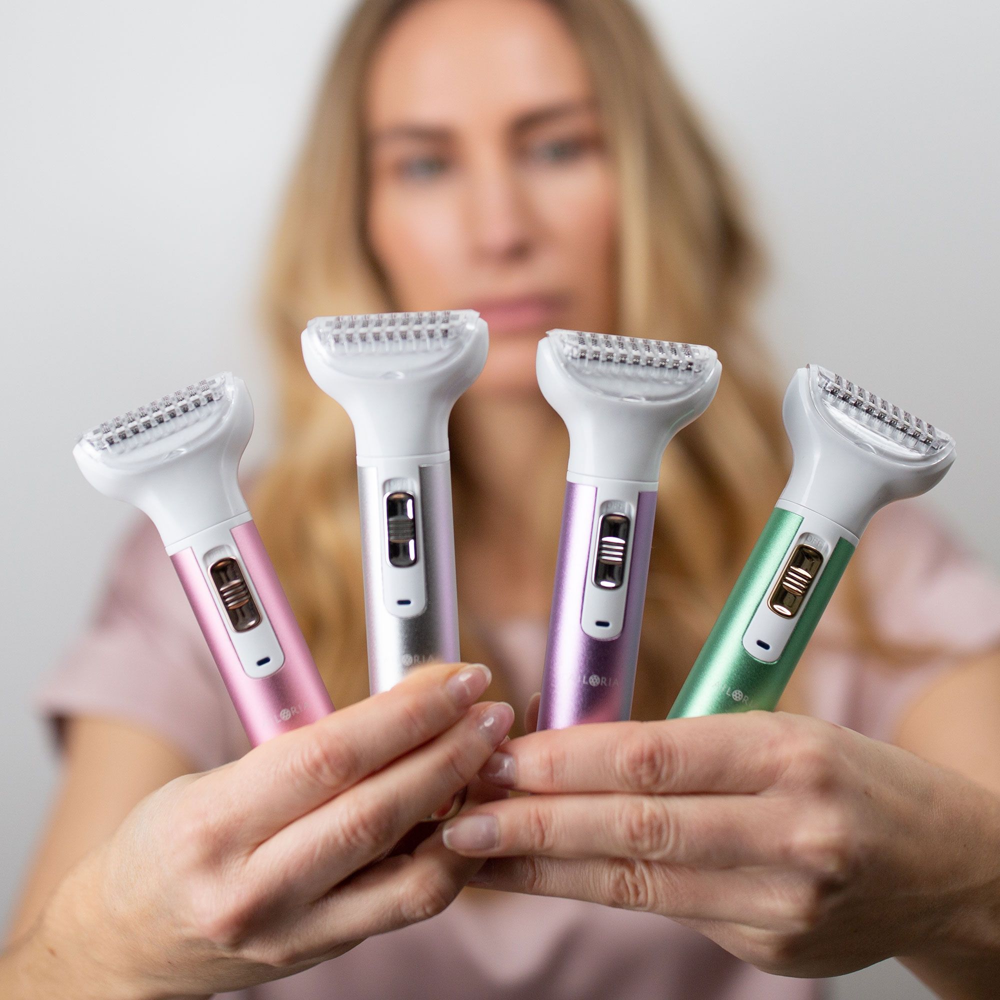 Quatre rasoirs avec manches colorées. Rose, argent, violet et vert. Une femme tient les rasoirs dans ses mains.