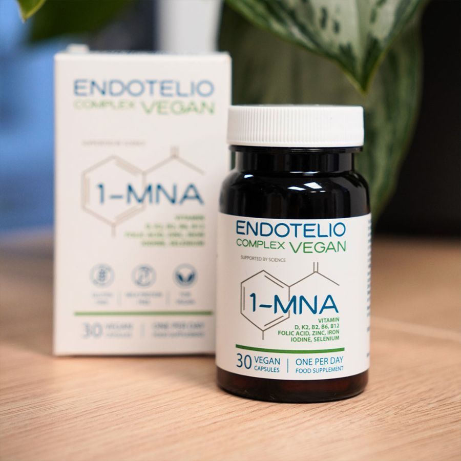 Bruine fles en doos met productinformatie. Opschrift: Endotelio Complex Vegan, 1-MNA, 30 capsules. Op een tafel, planten op de achtergrond.