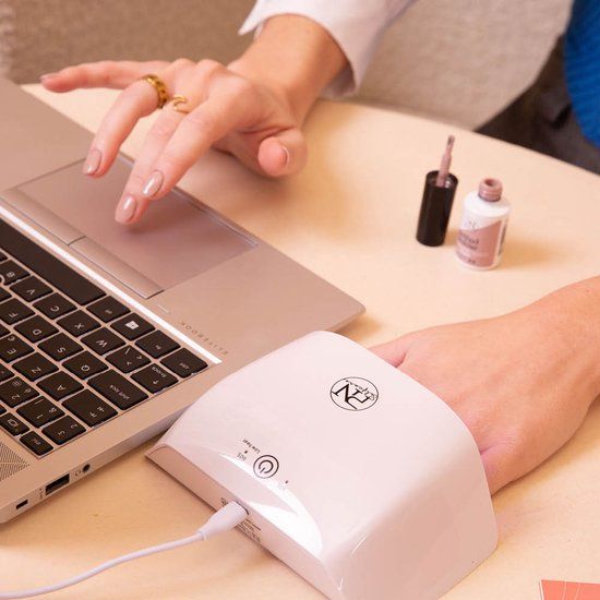 Main dans une lampe UV. Lampe blanche, logo PN. Ordinateur portable et flacon à côté. Câble USB.