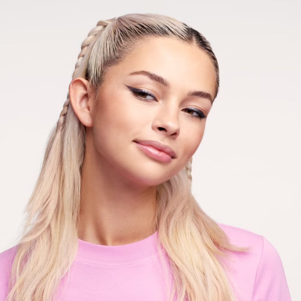 Portrait d'une jeune femme aux tresses blondes. Elle porte un haut rose et regarde sur le côté.