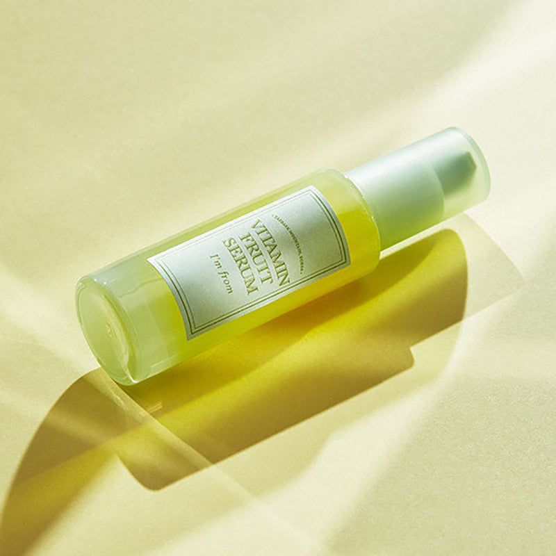 Serumfles op gele achtergrond. Opschrift: Vitamin Fruit Serum, I'm from. Schaduw.